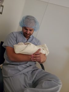 Father in theatre scrubs and hat holding his newborn baby