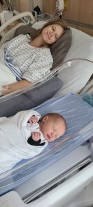 New mother in hospital bed with new baby lying in a clear sided hospital cot next to the bed