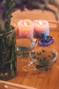 Candles, fresh lavender tea, purple and blue stone plus a vase with green stems on a wooden table